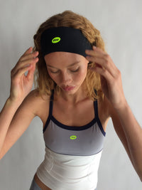 Woman wearing a black headband and sports outfit with visible branding on a plain background |M1
