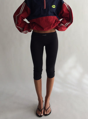 Person wearing a red and navy jacket with black capri pants on a plain background
