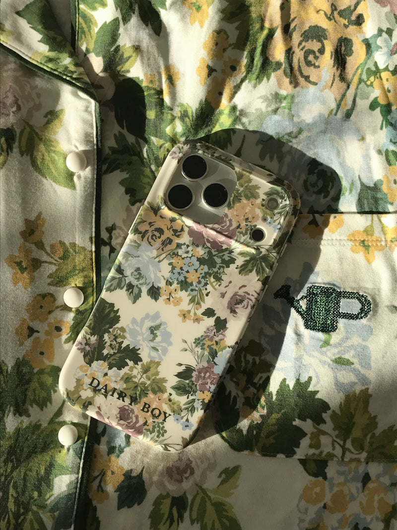 Phone case with a cream, blue, purple, yellow and green floral pattern and "DAIRY BOY" lettering, back view on floral pajamas.