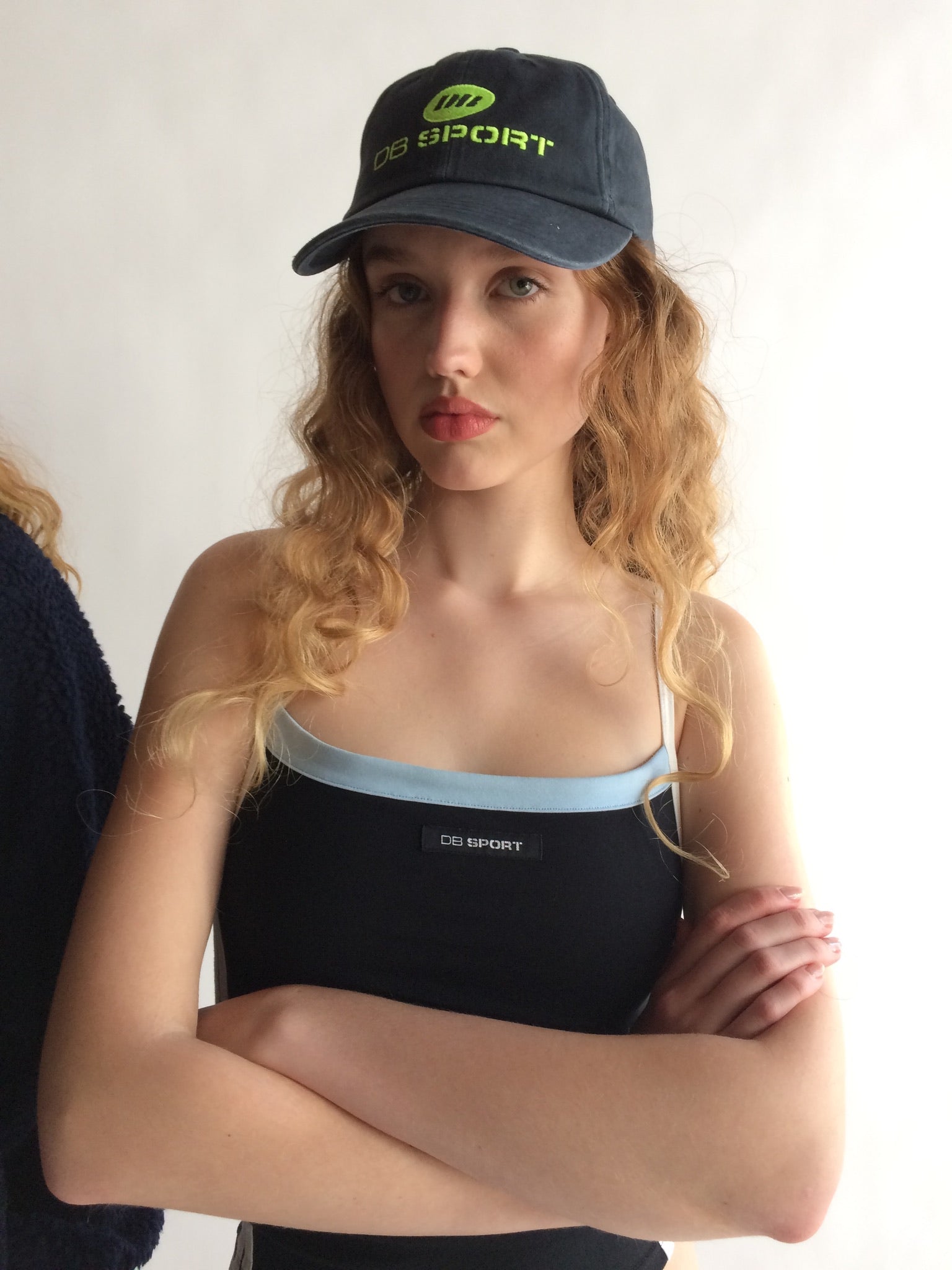 Woman wearing a black tank top and cap with visible DB SPORT branding against a plain background
