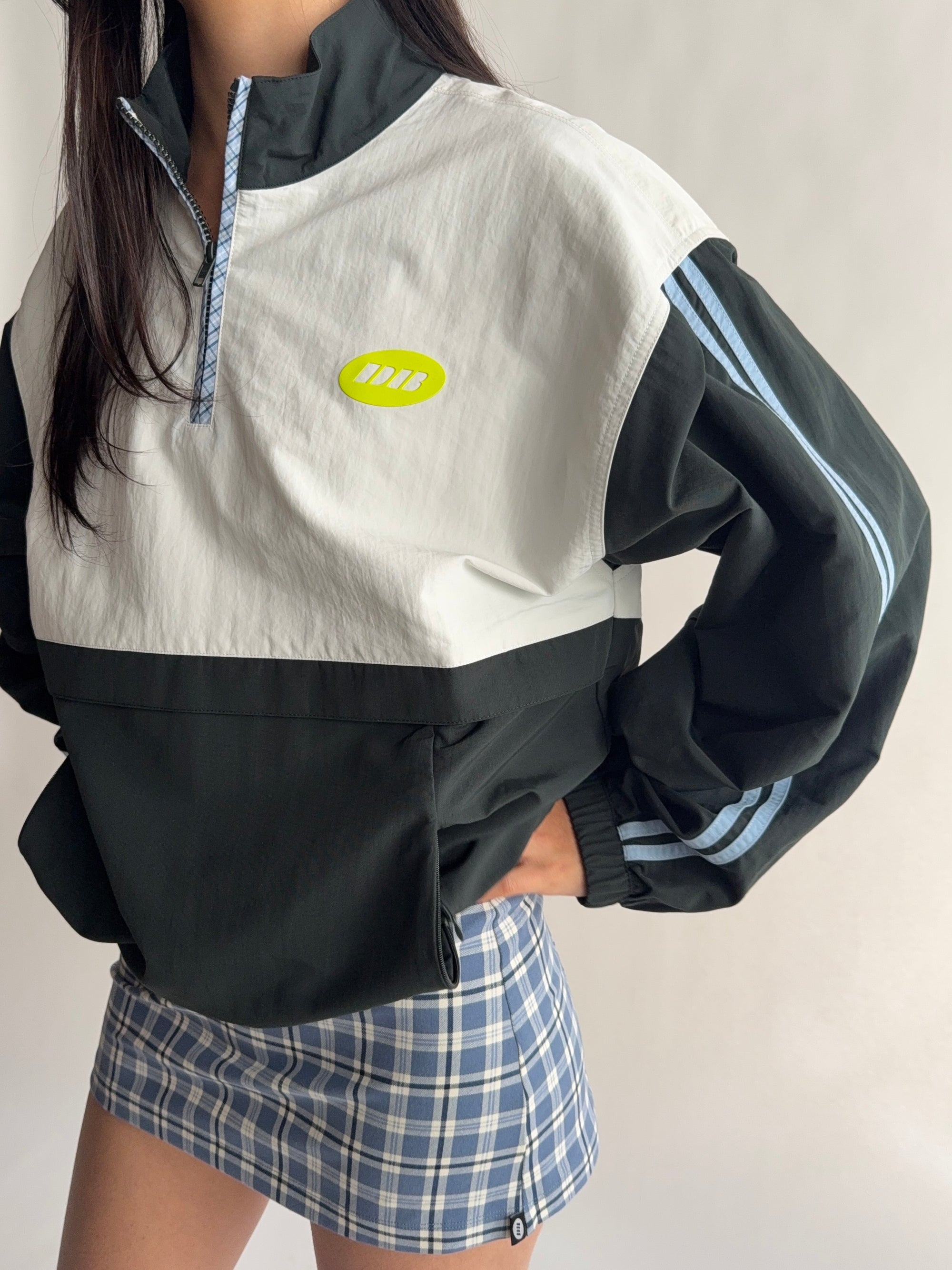 Person wearing a black and white jacket with a logo, standing against a plain background |M2