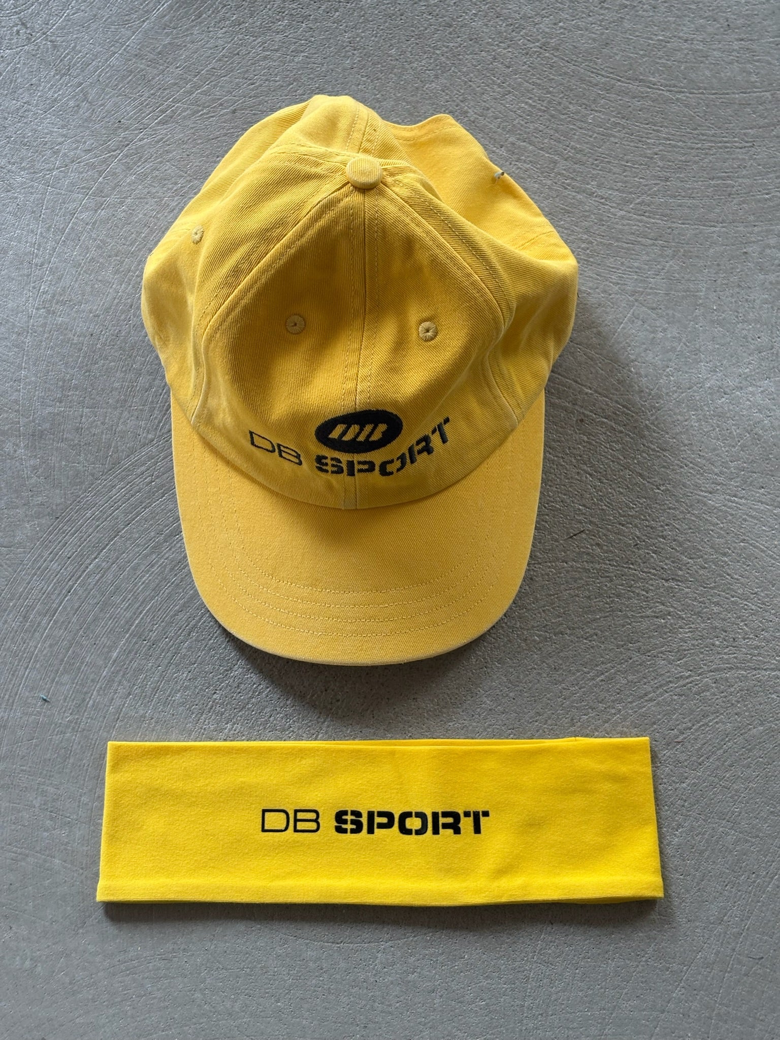 Yellow cap and headband with 'DB Sport' logo on a gray background