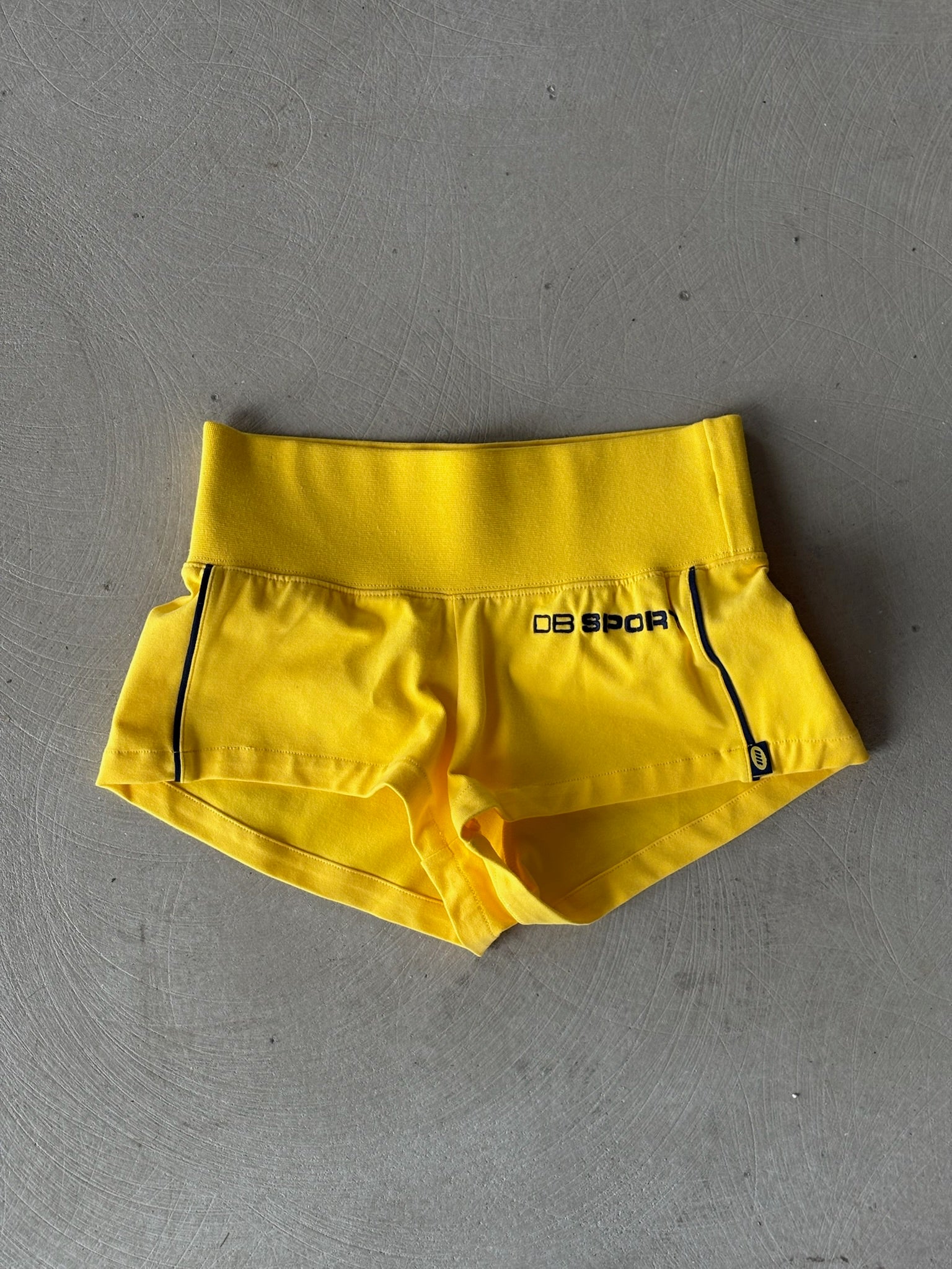 Yellow athletic shorts with a brand logo on a gray surface