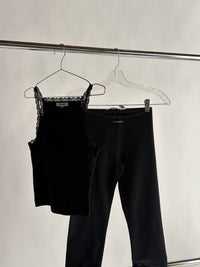 Black lace top and black pants hanging on a rack against a white background