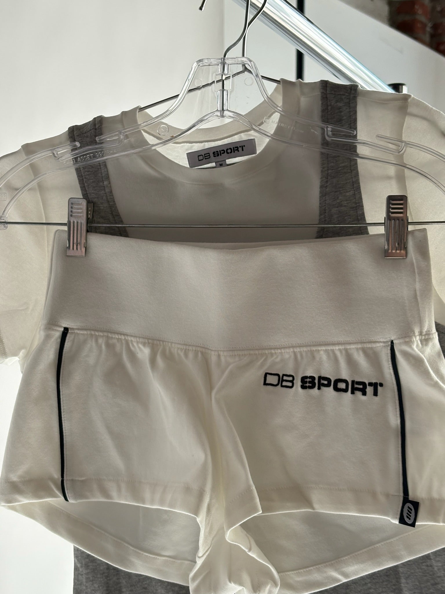 White athletic outfit with 'DB Sport' branding on a hanger against a white background