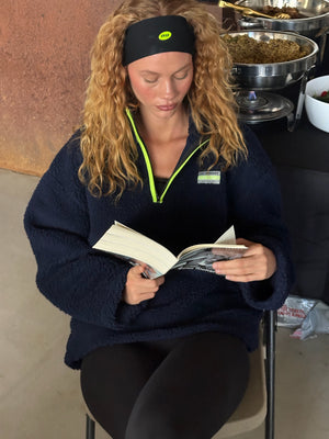 Woman reading a book in a casual setting with a headband and navy fleece.  |M1