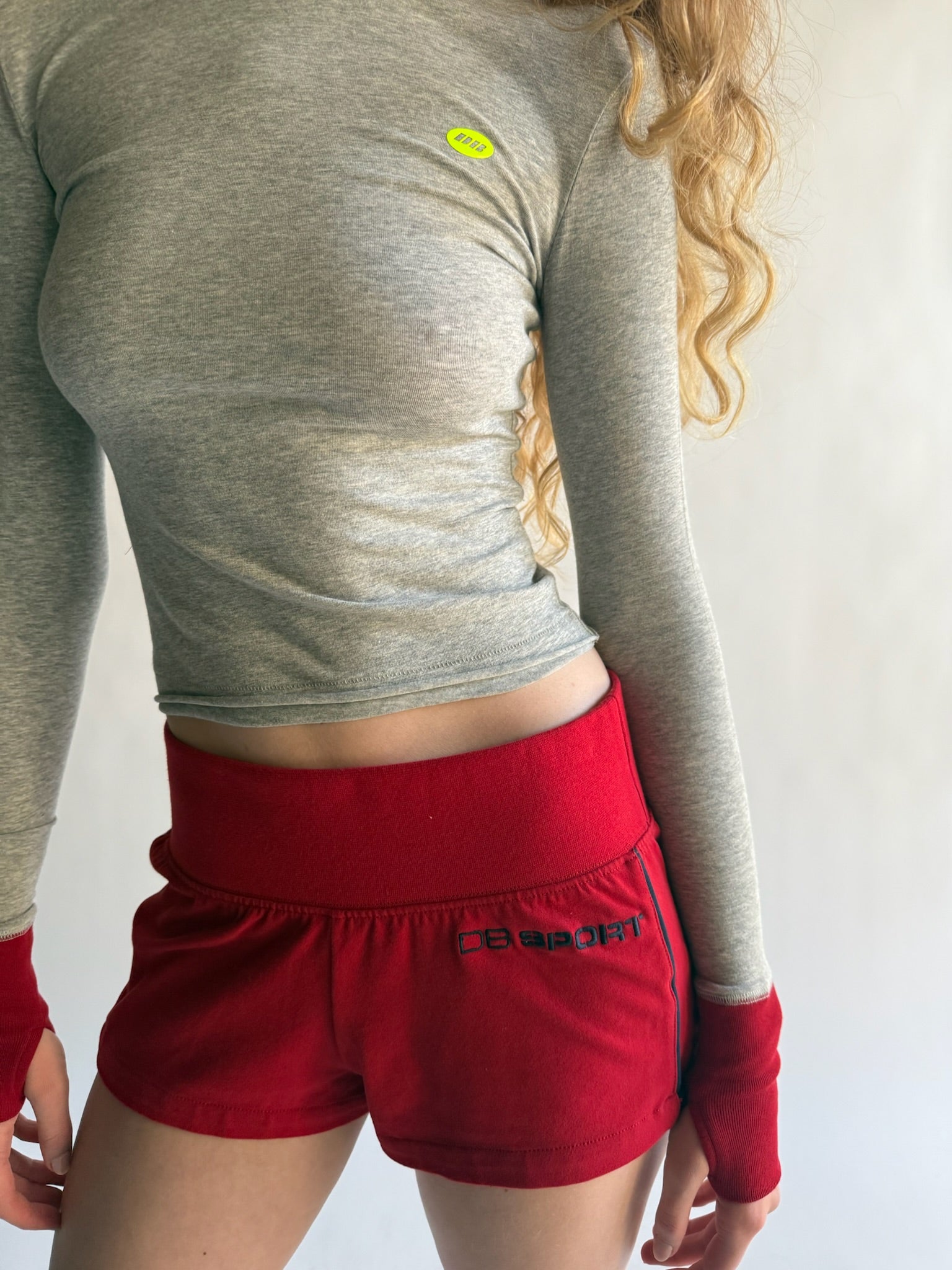Person wearing a gray long-sleeve top and red shorts with a visible brand logo.  |M1