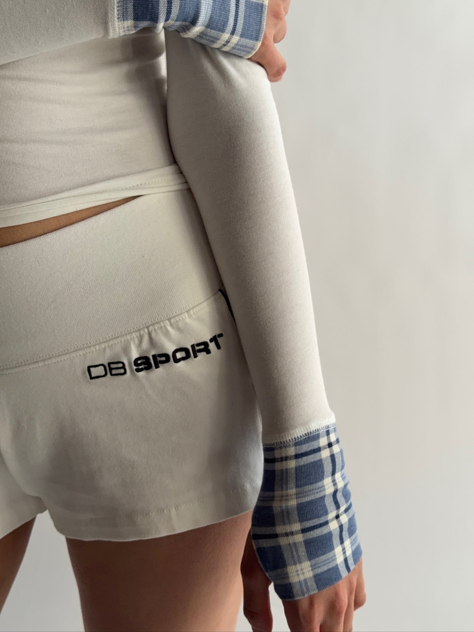 Person wearing a white long sleeve with 'DB Sport' logo and plaid sleeves with white DB sport shorts.  |M1