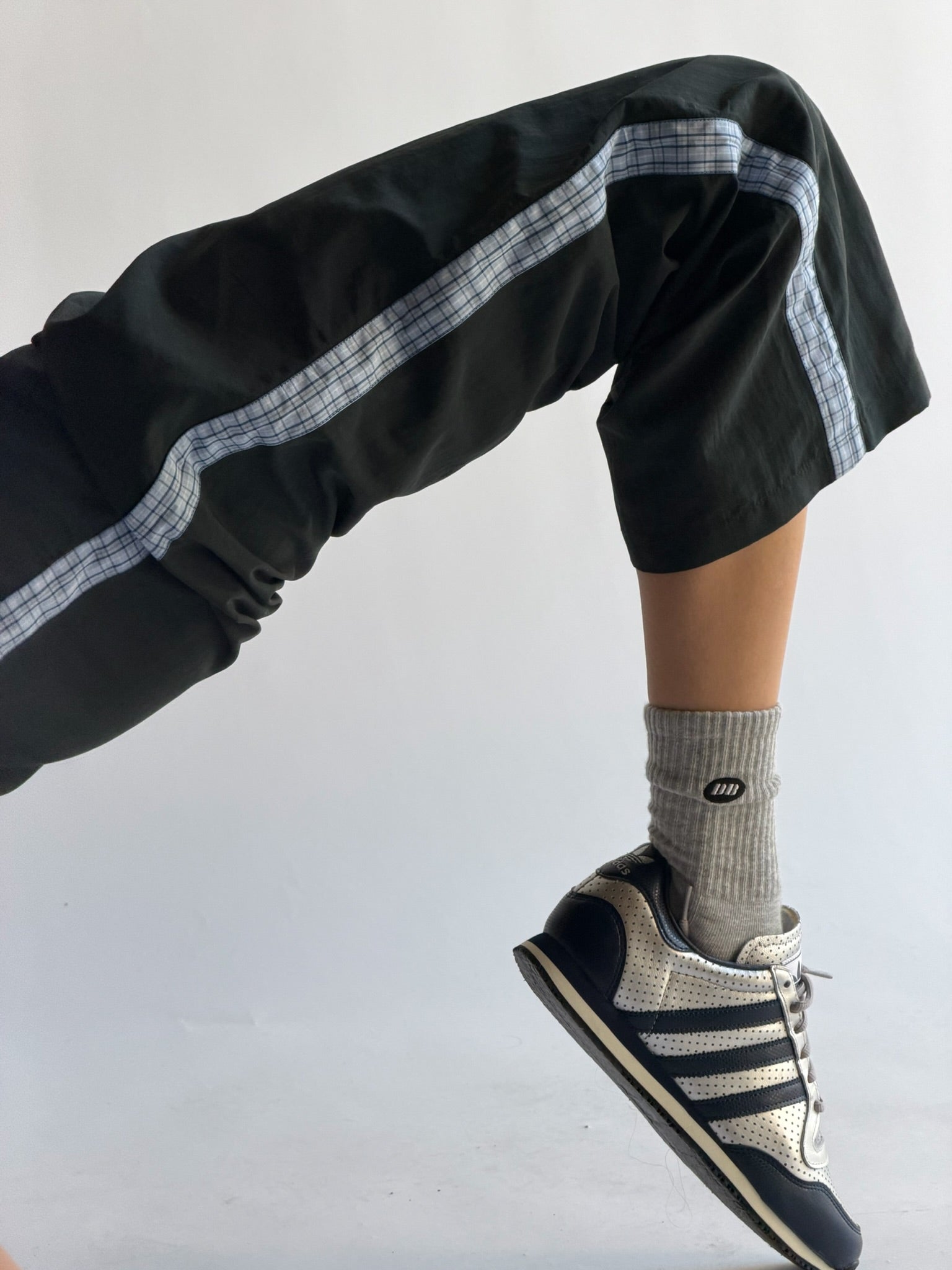 Person wearing black pants with white stripes, gray socks, and black sneakers on a light gray background