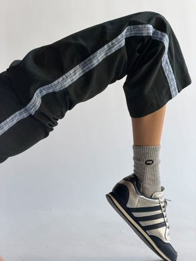 Person wearing black pants with white stripes, gray socks, and black sneakers on a light gray background