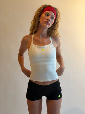 Woman wearing a white tank top and black shorts with a red headband against a plain background |M1