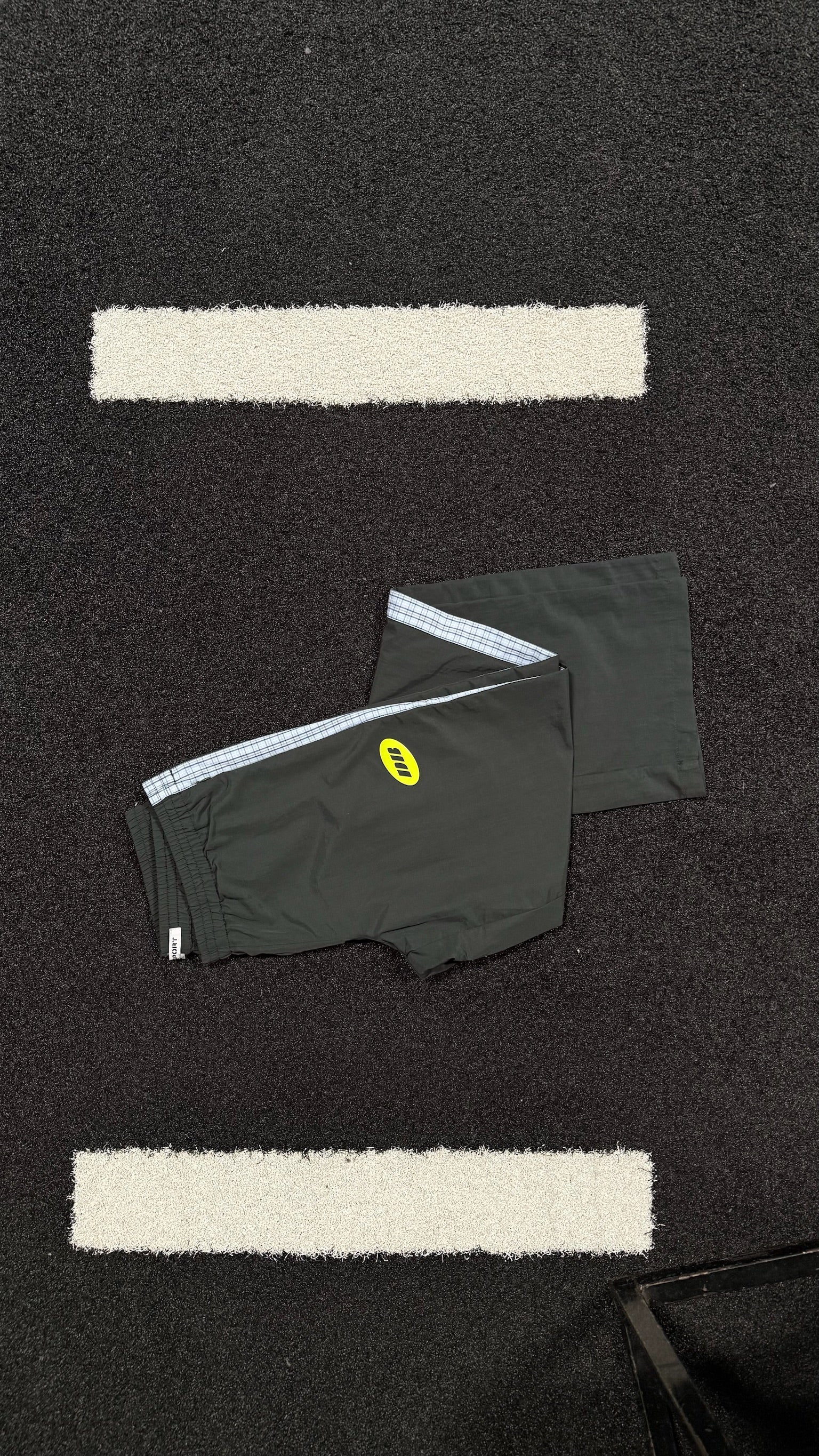 Black track pants with a logo on a black textured surface