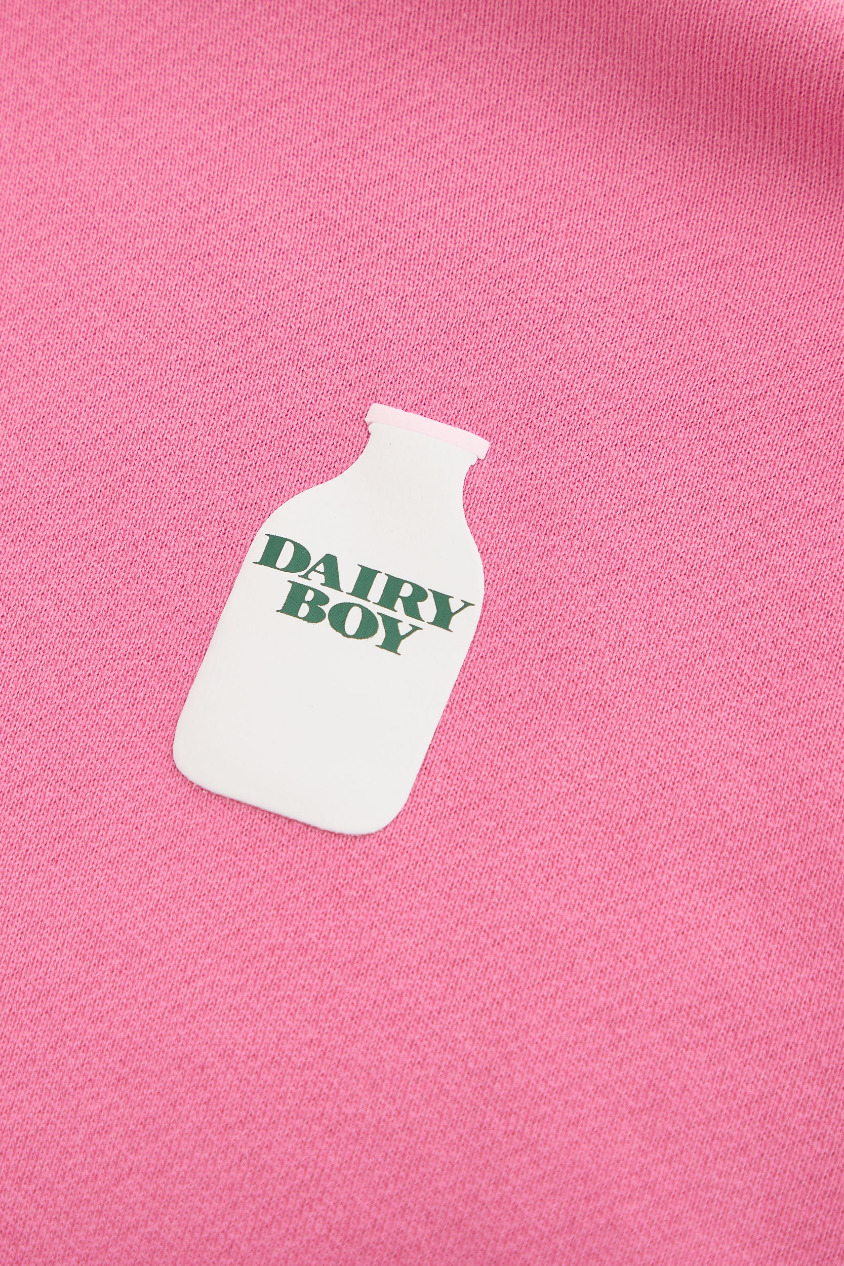 The Dairy Boy Strawberry Milk Bottle Zip Up features a white milk bottle graphic with "DAIRY BOY" in green, printed on strawberry milk-colored fabric.