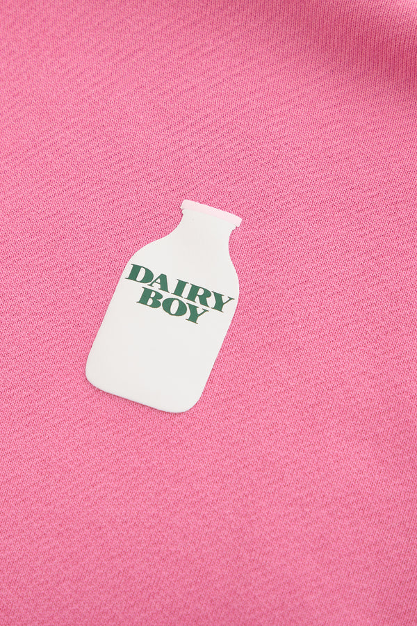 The Dairy Boy Strawberry Milk Bottle Zip Up features a white milk bottle graphic with "DAIRY BOY" in green, printed on strawberry milk-colored fabric.