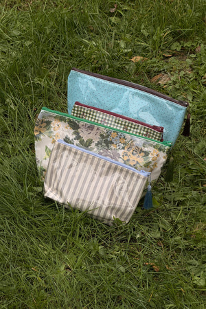 Light blue makeup bag with small dark dots, dark zip and tassel, shown at the back of a group of three other patterned pouches.