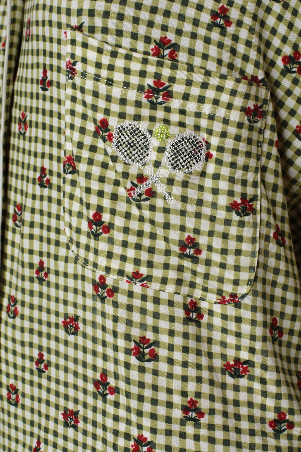Close-up detail of a sleep set shirt's chest pocket in green and white gingham with small red floral sprigs and a crossed tennis rackets motif.
