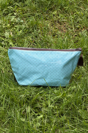 Light blue makeup bag with small dark dots, a brown zip across the top and a brown tassel on the pull, front view.