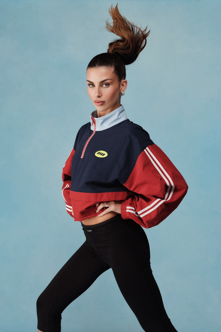 Woman wearing a red and navy jacket with a logo, posing against a blue background |M1